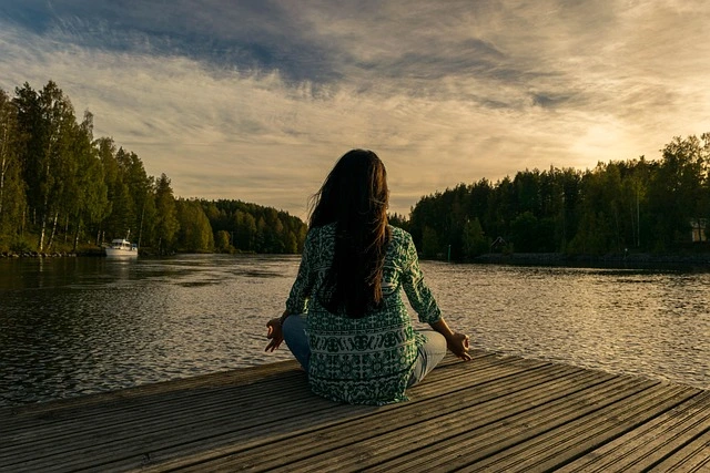 Une femme assise sur un ponton qui regarde l'horizon en faisant du yoga. Elle s'est abonné à Hors-ligne : le site de déconnexion